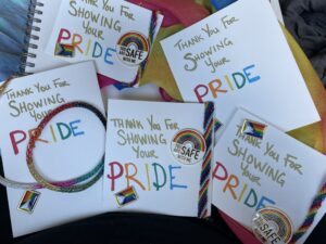 Prizes shown of a progressive pride viking wire weave necklace, a veil/scarf, pins and bracelets.